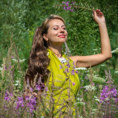 A radiant woman in a vibrant green dress enjoys nature in a lush summer meadow.