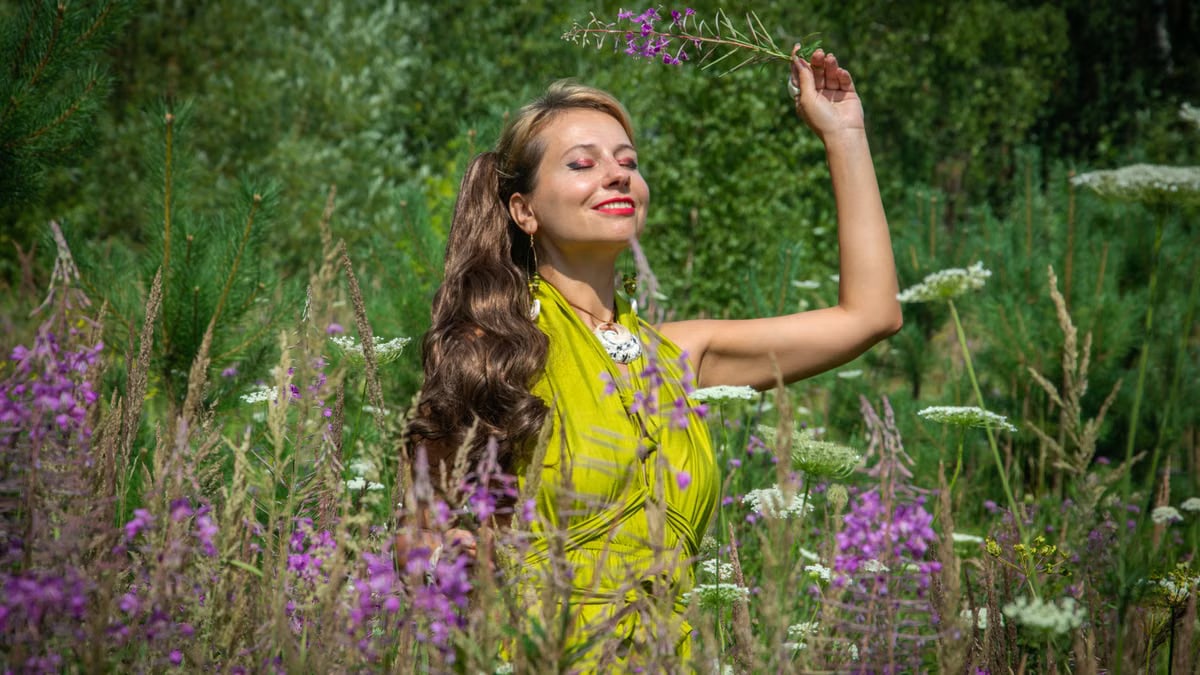 A radiant woman in a vibrant green dress enjoys nature in a lush summer meadow.